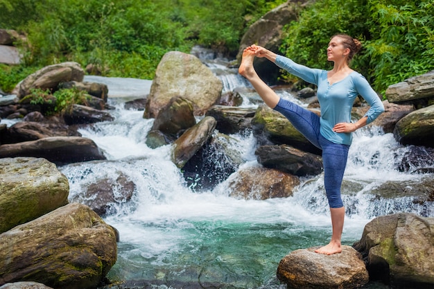 Woman doing Ashtanga Vinyasa Yoga asana outdoors at waterfall