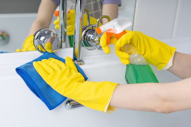 Woman doing chores in bathroom cleaning bathtub with spray and cloth