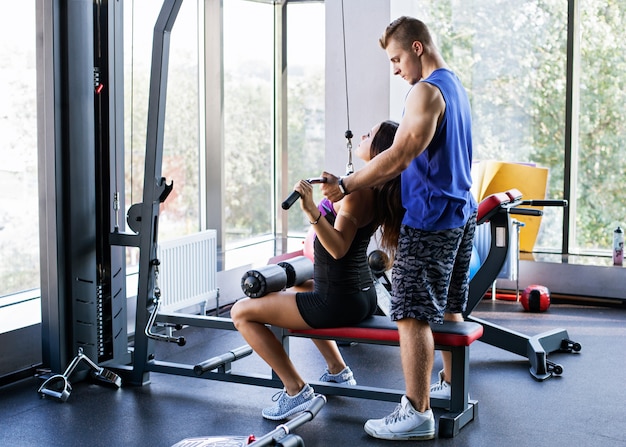 Woman doing pull down exercise for the back under a personal trainer's