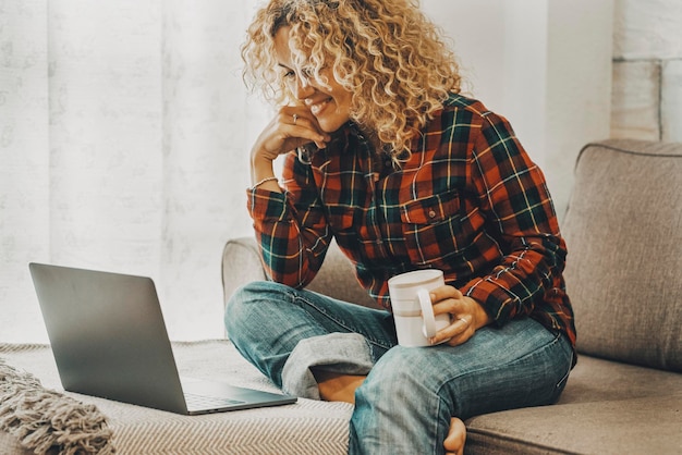 Woman doing video call conference comfortably sitting on the sofa at home in technology leisure activity Female using computer on the couch Modern online people enjoy internet connection and smile