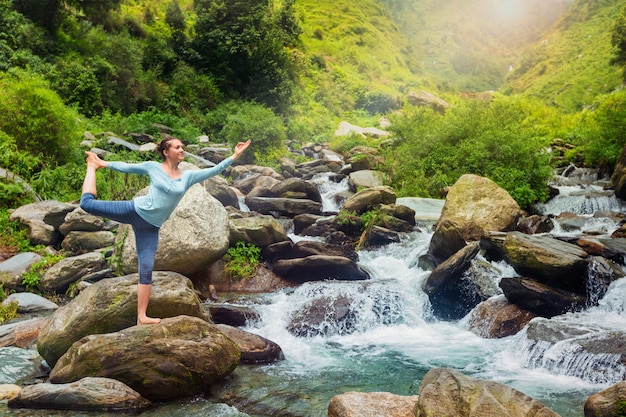 Woman doing yoga asana Natarajasana outdoors at waterfall