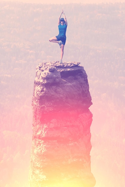 Woman doing yoga at the peak of a great rock in a forest Toned