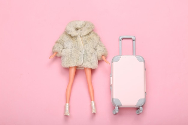 Woman Doll in fur coat and shoes with luggage on pink background Minimalism fashion and travel layout Top view Flat lay