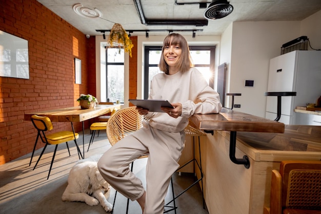 Woman in domestic wear sitting with digital tablet in modern home studio