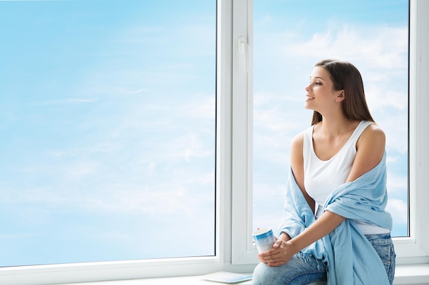 Woman Dreaming looking at Window Girl thinking and enjoying Morning Cup of Coffee Resting at Home