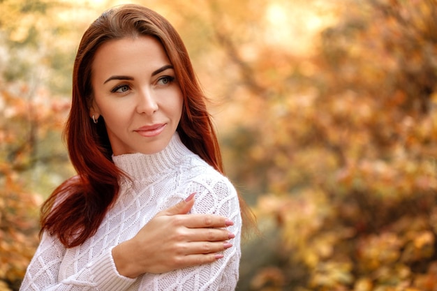 Woman in dress and hat on background of autumn foliage