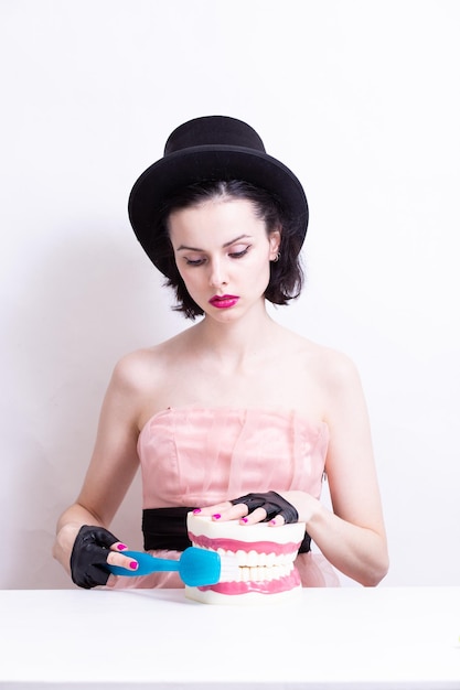 A woman in a dress and hat sits at a table and holds a mockup of her teeth High quality photo