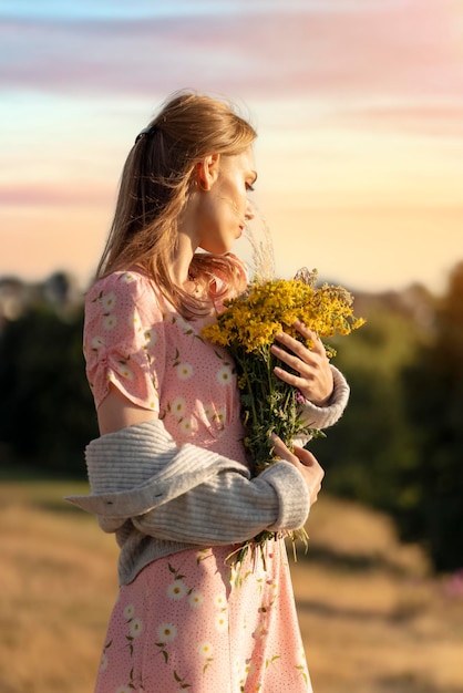 Woman in a dress and a hat with a lavender bouquet in her hands on a hill in summer sunset