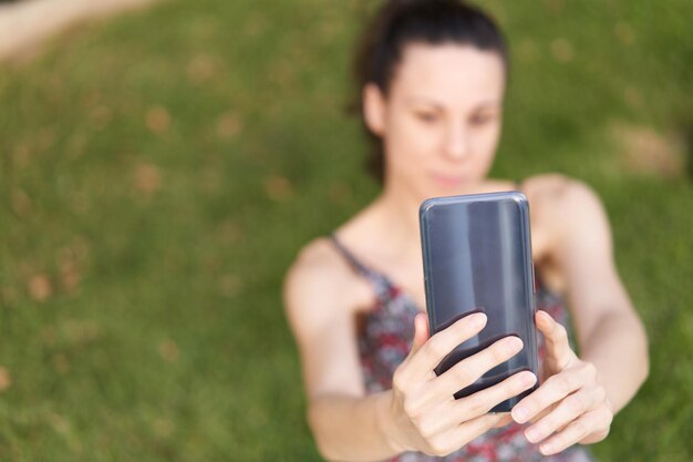 Woman in dress smiling taking a selfie on the grass