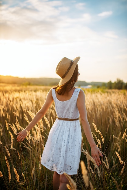 Woman in dress walking in wheat field on sunset