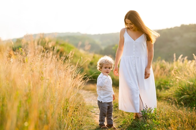 Woman in dress walks in nature with her son with curly hair