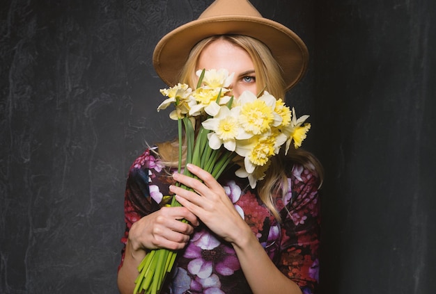 Woman in dress with a bouquet of daffodils in her hands looks through a bouquet