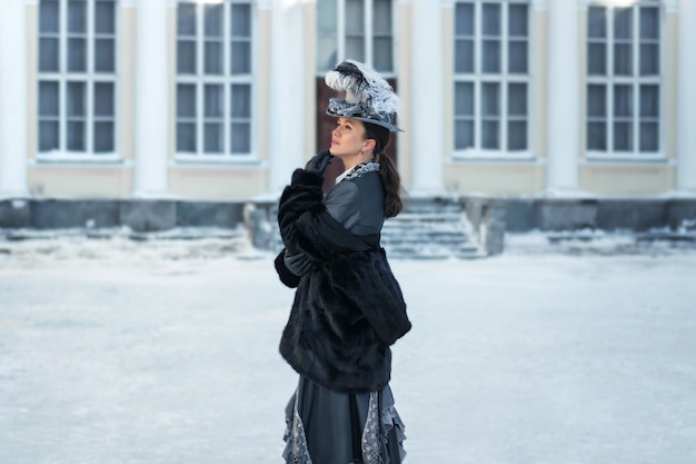 A woman dressed as a 19th-century noblewoman stands outside the castle.winter in russia