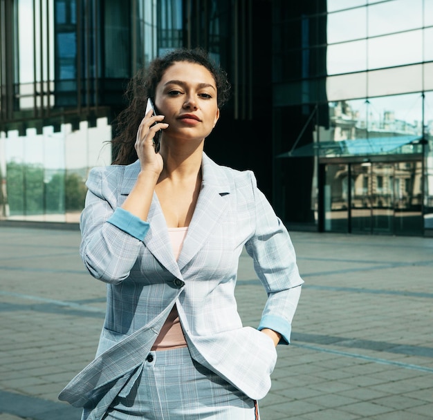 Woman dressed in business style against the background of a business center is holding a mobile phone