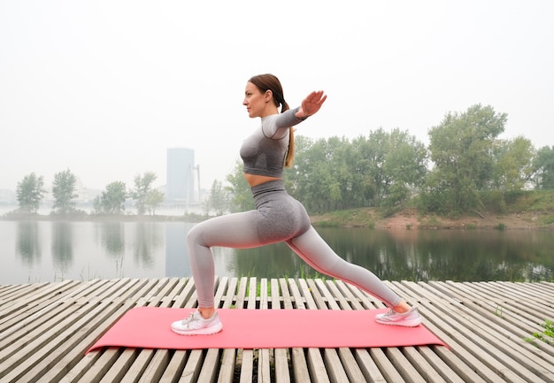 Woman dressed leggings and top with pink mat doing yoga on summer park.Healthy sport lifestyle concept