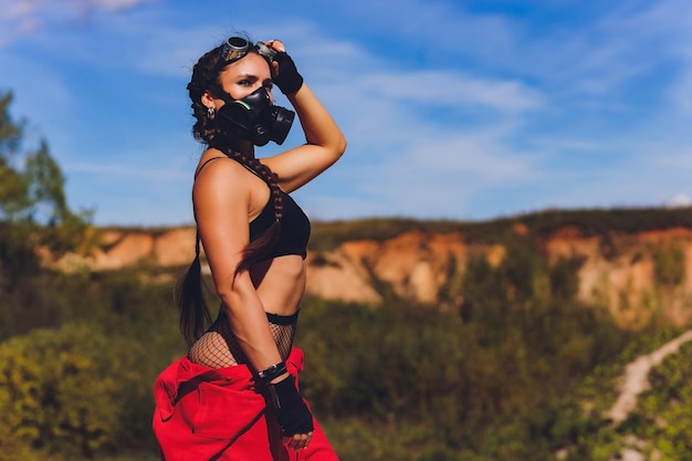 Woman dressed in a steampunk suit in a defiant attitude with her arms crossed respirator on the face against the background of a dirty lake