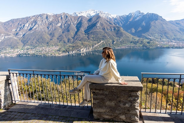 Woman dressed in white sitting on terrace looking at snow capped mountains in Lago di Como Italy