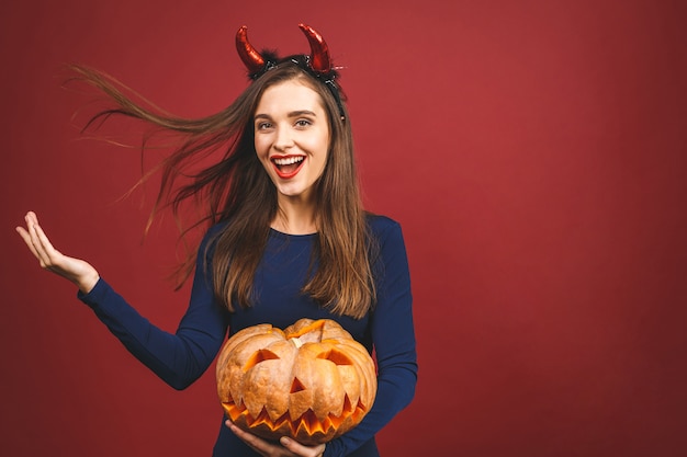 Woman dressing in black devil Halloween costume with witch's headband for a themed party. She hold pumpkin for a 'trick or treat'