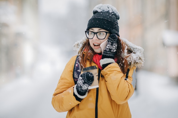 Woman drinking coffee and talking on the phobne outside in winter