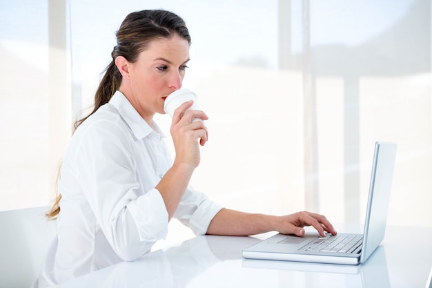 woman drinking a coffee and typing at her desk