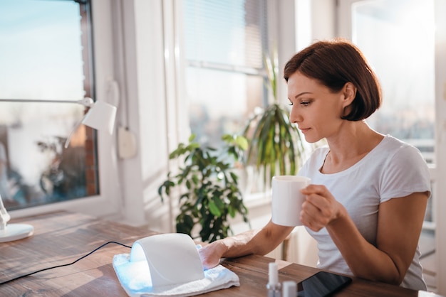 Woman drinking coffee while drying nails