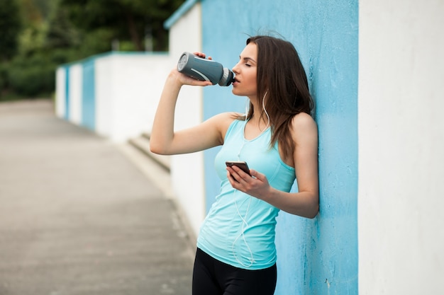 Woman drinking from a canteen and holding a phone