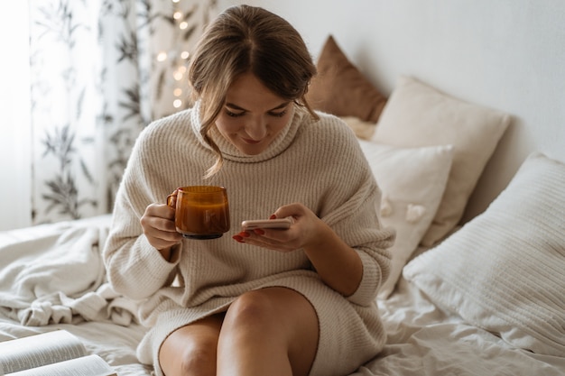 Woman drinking hot tea and using phone. Comfy lifestyle.