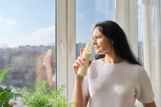 Woman drinking milk drink from bottle standing near window milk yogurt dairy healthy drinks