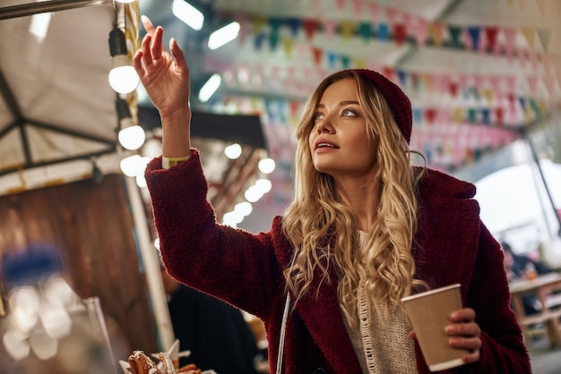 Woman drinking mulled wine at the street food market she shows something