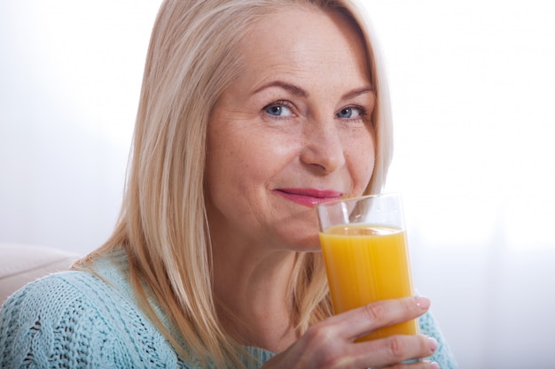 Woman drinking orange juice smiling. Beautiful middle aged Caucasian model face closeup.