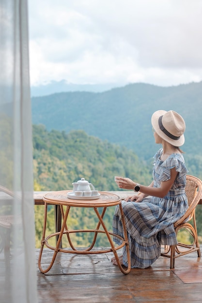 Woman drinking tea and looking mountain view, young blogger stay at countryside homestay in the morning.Travel, vacation, journey, trip and relaxing concept