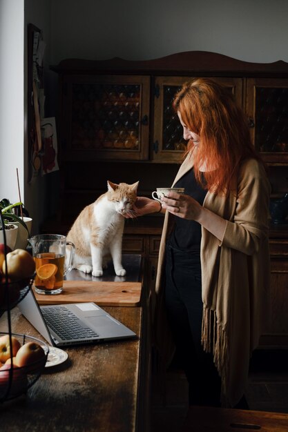 Woman drinking tea and stroking ginger cat at retro home