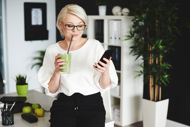 Woman drinking vegetable juice and using mobilephone