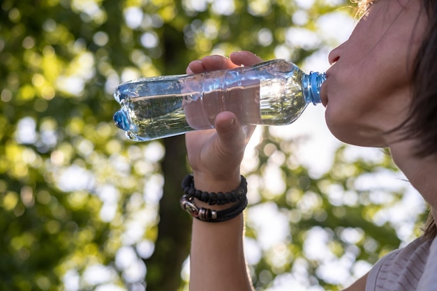 Woman drinks cool drinking water from a plastic bottle on a hot day