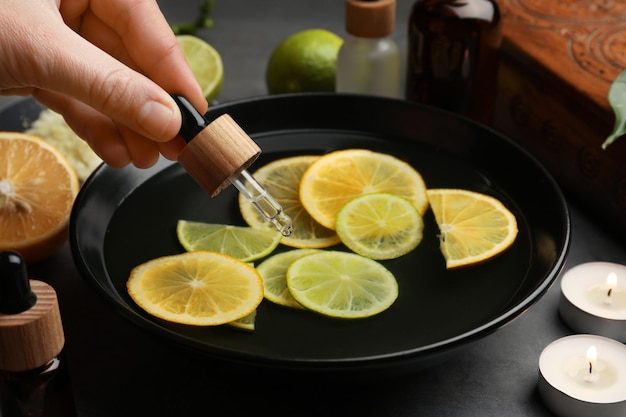 Woman dripping essential oil into bowl with lemons at grey table closeup Aromatherapy treatment