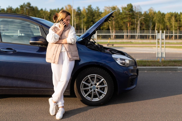 A woman driver calls a tow truck on the phone due to a car breakdown on the road