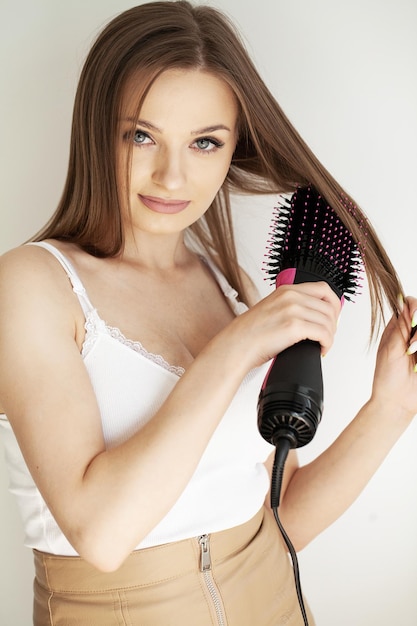 Woman drying long brown hair with blow dryer and round brush