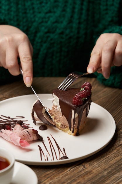 Woman eating chocolate cake with raspberry. Woman hands cutting chocolate mousse cake with raspberry