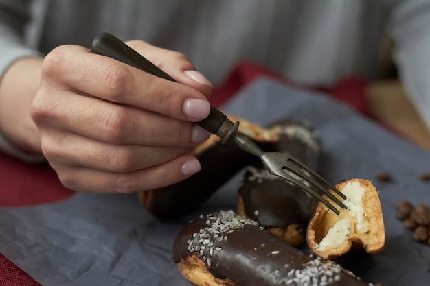 Woman eating eclairs filled with cream, traditional french eclairs with chocolate and cup of espresso.