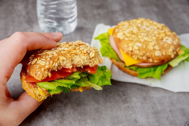 Woman eating english muffins sandwiches with ham, tomatoes and lettuce.