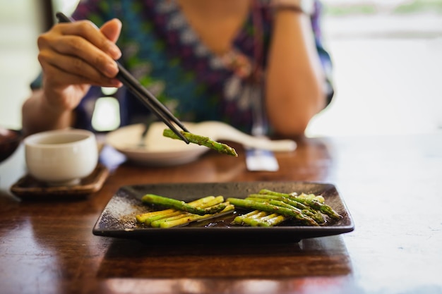 Woman eating grill asparagus with wooden chopsticks in restaurant