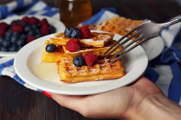 Woman eating Sweet homemade waffles with forest berries and sauce closeup