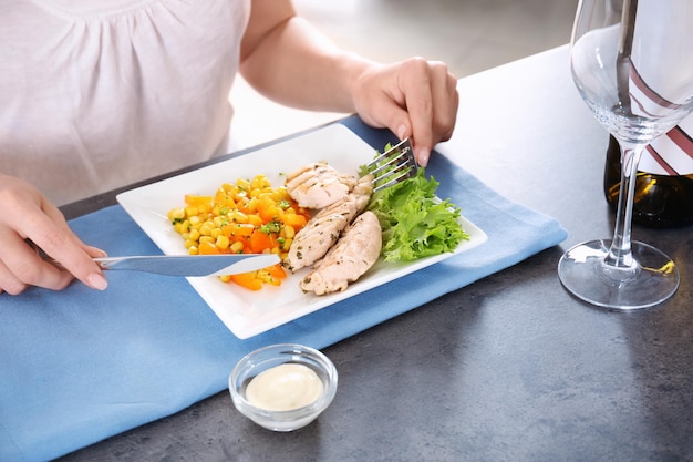 Woman eating tasty chicken meat with vegetables on table in kitchen Cooking for one concept