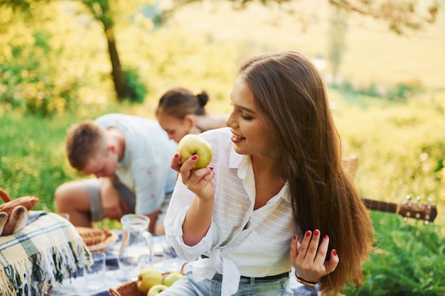 Woman eats apple Group of young people have vacation outdoors in the forest Conception of weekend and friendship