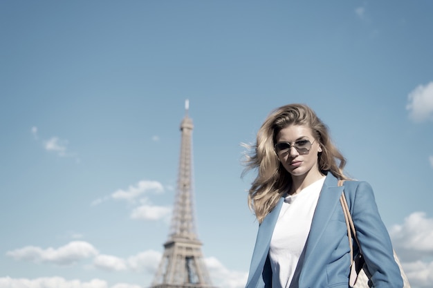 Woman at eiffel tower in paris, france on blue sky. Girl traveler in sunglasses, jacket on sunny summer day outdoor. Architecture, attraction, landmark. Vacation, travelling, wanderlust, france