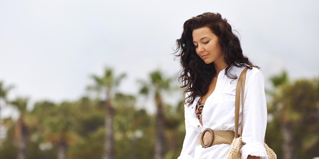 Woman in elegant beach outfit outdoors against palm trees on the background during summer