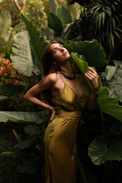 woman in elegant silk dress posing in tropical rainy tropical forest.