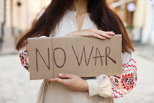 Woman in embroidered dress holding poster No War on city street closeup