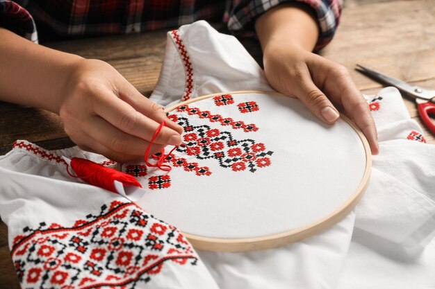 Photo woman embroidering white shirt with colorful threads at wooden table closeup ukrainian national clothes