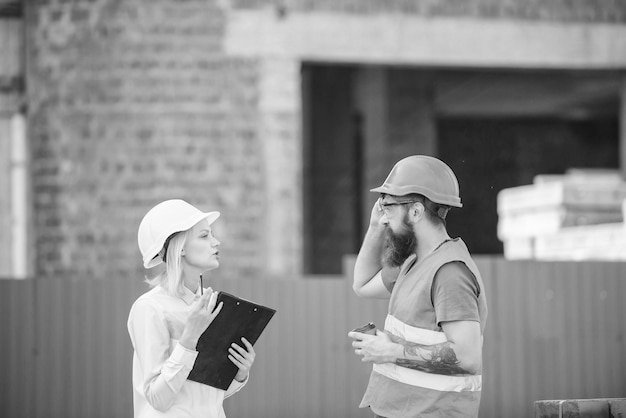 Woman engineer and bearded brutal builder discuss construction progress Construction industry concept Relationships construction client and participant building industry Discuss progress plan